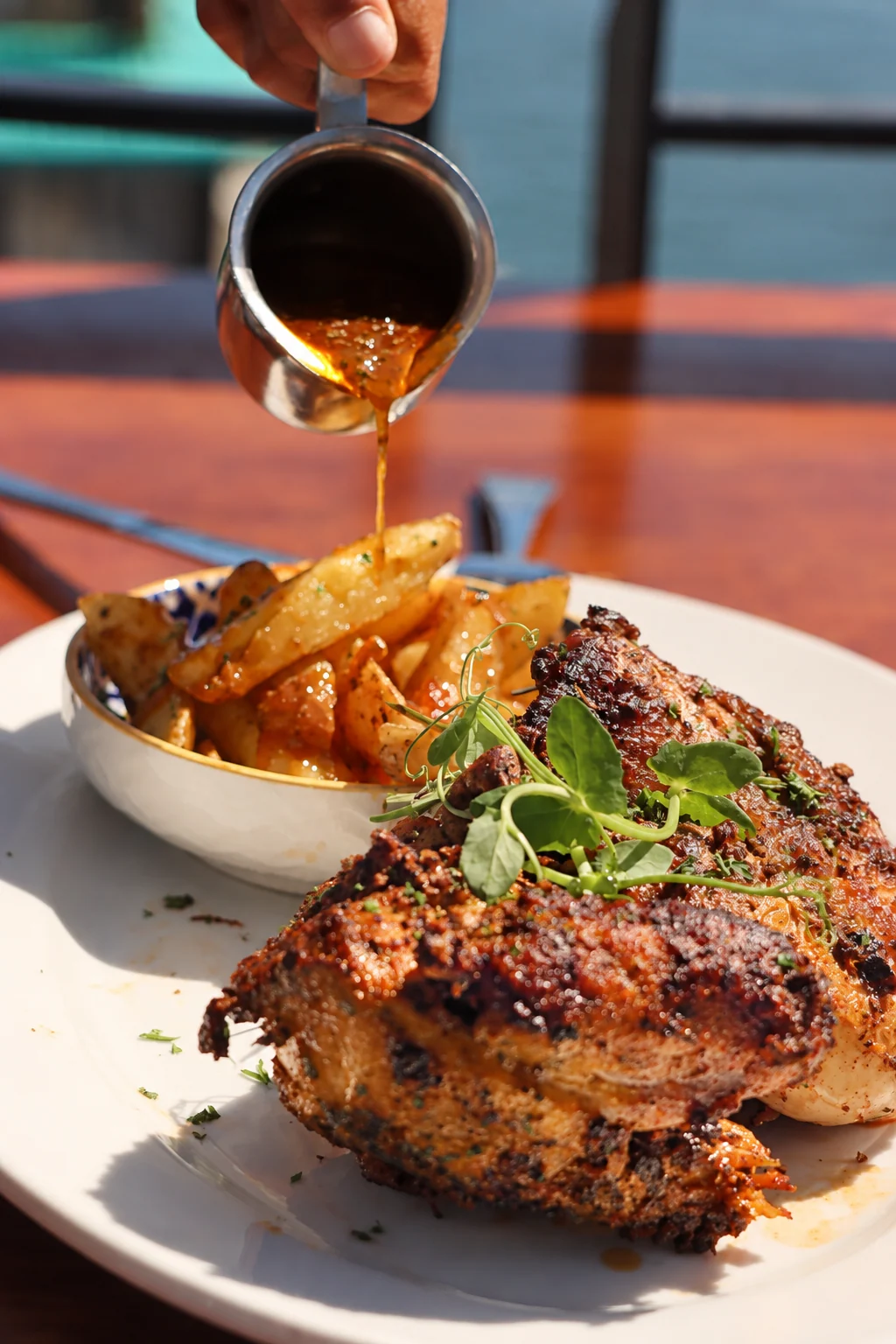 Sauce poured over golden potatoes beside grilled chicken and fresh herbs