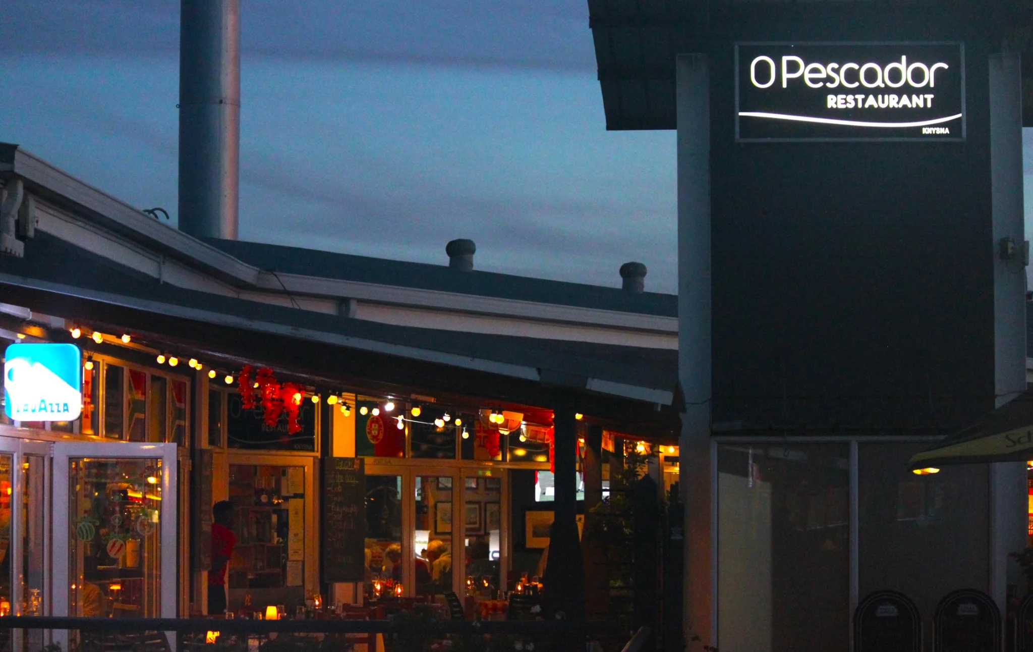 O Pescador illuminated sign and warmly lit dining room at dusk