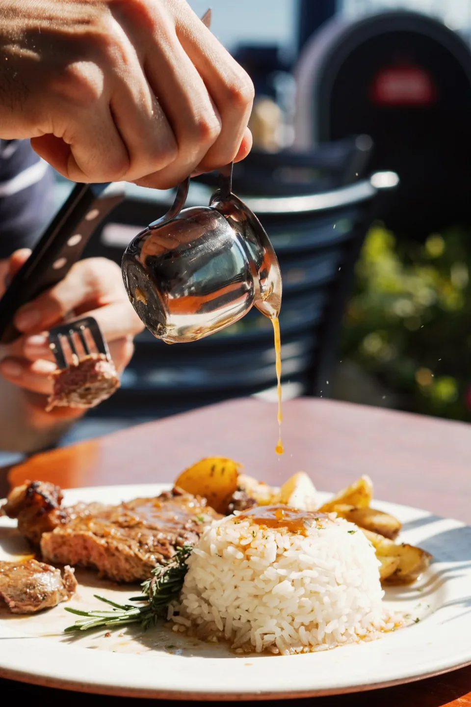 Sauce being poured at the table over rice beside grilled meat and golden potatoes